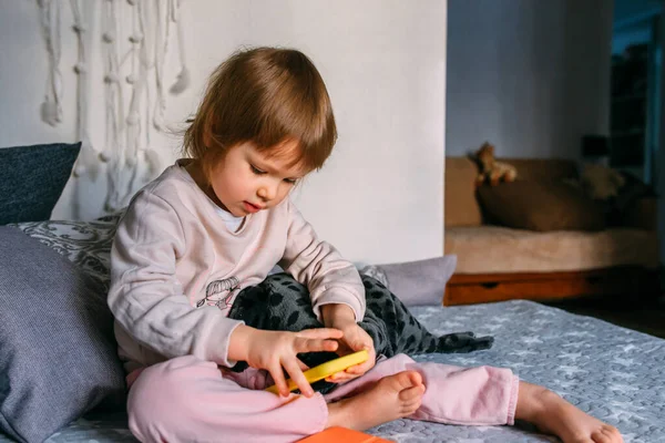 Kanepede oturan küçük bir çocuk akıllı telefon kullanıyor. — Stok fotoğraf