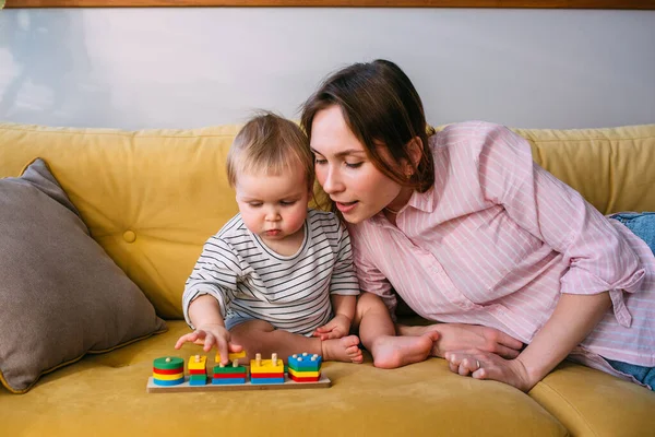 Mamãe brinca em casa com uma criança pequena no sofá, divirta-se. — Fotografia de Stock