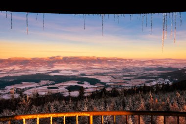 Gün batımında dağlarda kış manzarası, karla kaplı dağ tepeleri ve orman, gözlem kulesinin manzarası..