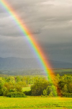 Dağların üzerinden sayısız yağmur yağışı geçen bir fırtına, bulutların arkasından güneş doğdu, kara bulutların arka planında renkli bir gökkuşağı..