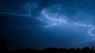 Yaz fırtınası sırasında elektrik boşalımı, gece gökyüzünde dallanmış yıldırımlar..