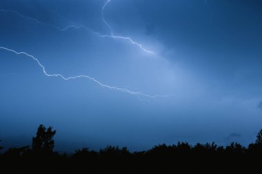 Yaz fırtınası sırasında elektrik boşalımı, gece gökyüzünde dallanmış yıldırımlar..