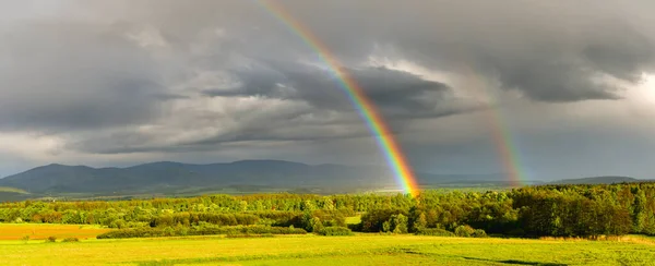 Dağların üzerinden sayısız yağmur yağışı geçen bir fırtına, bulutların arkasından güneş doğdu, kara bulutların arka planında renkli bir gökkuşağı..