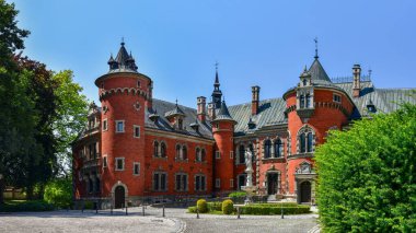 The Palace in Plawniowice, the palace and park complex from the 1980s. A magnificent building made of red brick with numerous decorations, the view on a sunny summer day.