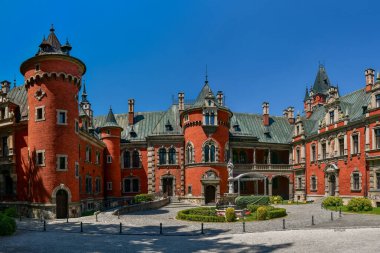 The Palace in Plawniowice, the palace and park complex from the 1980s. A magnificent building made of red brick with numerous decorations, the view on a sunny summer day.