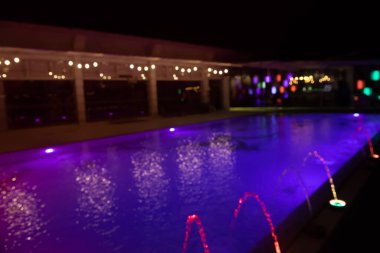 Abstract blurred of colorful lightbulb bokeh around swimming pool with fountain at night, can be used for Christmas or new year party background