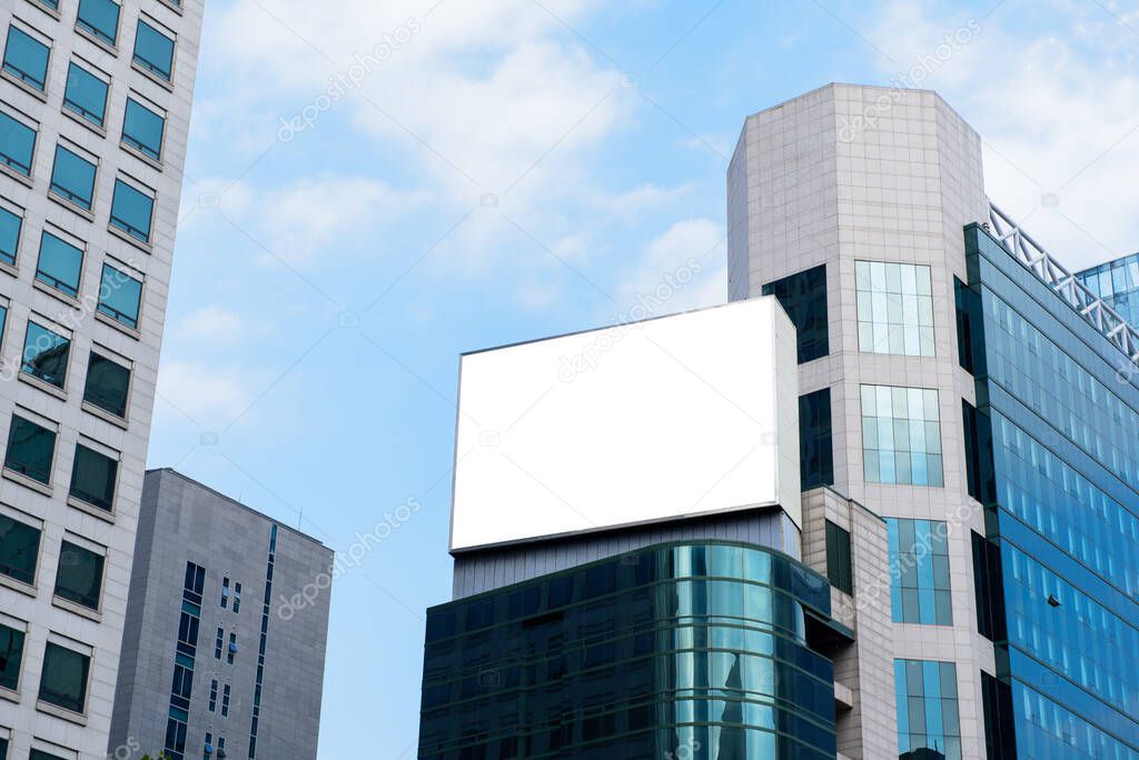 Blank advertising billboard on top of modern building in the city with blue sky background useful for products advertisement