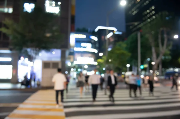 Blurred people crossing the street in the city at night with cars, traffics light, colorful bokeh and buildings as background