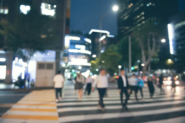 Blurred people crossing the street in the city at night with cars, traffics light, colorful bokeh and buildings as background