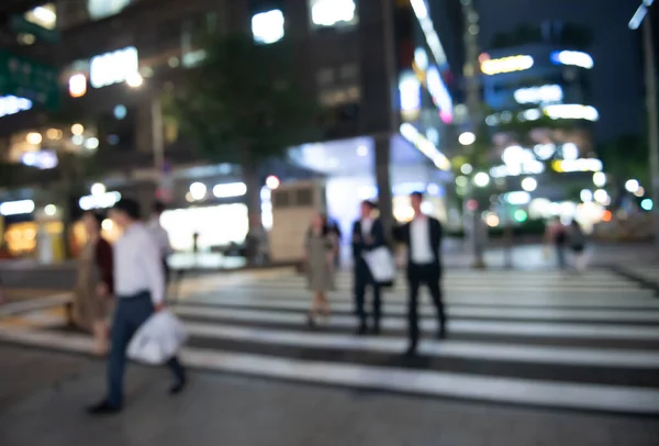 Blurred people crossing the street in the city at night with cars, traffics light, colorful bokeh and buildings as background