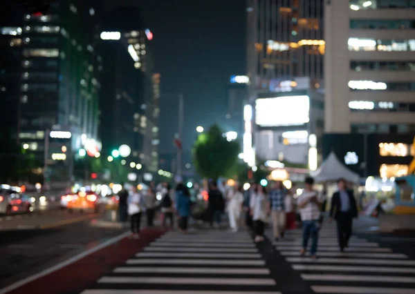 Blurred people crossing the street in the city at night with cars, traffics light and buildings as background, Night life in Korea