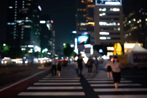 Blurred people crossing the street in the city at night with cars, traffics light and buildings as background, Night life in Korea