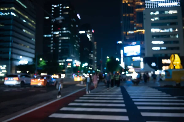 Blurred people crossing the street in the city at night with cars, traffics light and buildings as background, Night life in Korea