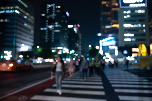 Blurred people crossing the street in the city at night with cars, traffics light and buildings as background, Night life in Korea