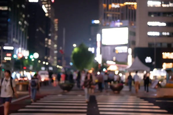 Blurred people crossing the street in the city at night with cars, traffics light and buildings as background, Night life in Korea