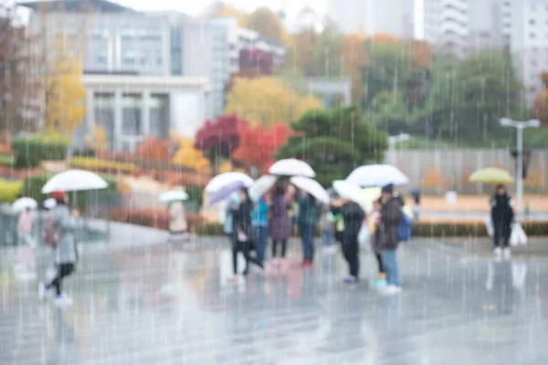 Walking in the rain. Abstract blurred, Crowd people with umbrella walking on pedestrian in university, raining with colorful autumn leaves background.