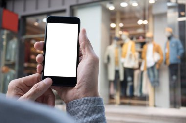 Şehirdeki alışveriş merkezinde arka planda bulanık moda mağazası olan boş ekran cep telefonu kullanan bir adam.