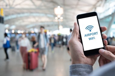 Airport free WiFi zone. Man using mobile smart mobile phone connecting airport free wifi, passenger walking with baggage as background, internet airport service