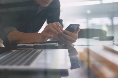 Asian business man using mobile phone, busy working on laptop computer with calculator, financial document on desk in modern office, business strategy analysis, work process concept, close up