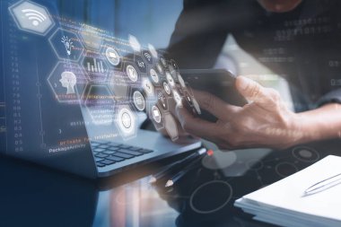 İş teknolojisi, IoT Internet of Things, yazılım geliştirme konsepti. İş adamı, web tasarımcısı dizüstü bilgisayar ve cep telefonu üzerinde çalışıyor. Programcı mobil uygulamalar geliştiriyor. Web simgeleri, bilgisayar kod arayüzü