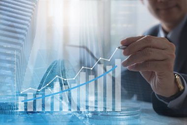Ticari mali yatırım ve teknoloji konsepti, finansal grafiği analiz eden başarılı iş adamının çifte maruziyeti, bozuk paralar ve şehirdeki modern binalar ofisi ile sanal ekranda ekonomik büyüme
