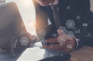 İş ve modern teknoloji, yazılım geliştirme, BI İş Zekası kavramı. İş adamı cep telefonu kullanıyor, ofisteki dizüstü bilgisayarda sanal ekranda teknoloji simgeleriyle çalışıyor.