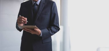 Takım elbiseli bir işadamı, dijital tablet bilgisayar ve stilus kalem kullanan yönetici beyaz modern ofis içi arka plan ve kopyalama alanına not alıyor. İş ve teknoloji kavramı