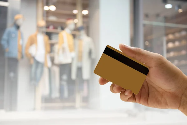 Man hand holding empty golden credit or debit card, member card, vip card with magnetic stripped over blurred background of fashion boutique in department store, credit card payment concept.