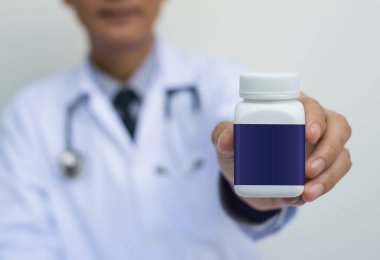 Beyaz üniformalı erkek doktor elinde mavi boş ilaç şişesi, kapat.