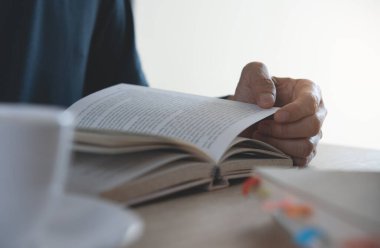 Kitap okuyan bir öğrencinin yakın plan resmi. Sıradan bir iş adamı, ana ofiste kahve molası sırasında, bir fincan kahveyle rahatlamış bir şekilde kitap açıp kitap okuyor..