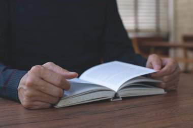 Genç Asyalı bir adamın kitap okurkenki görüntüsü. Sıradan bir adam, öğrenci açılışı ve gevşetilmiş kitap üniversite kütüphanesinde ahşap masanın üzerinde, klasik tarzda..
