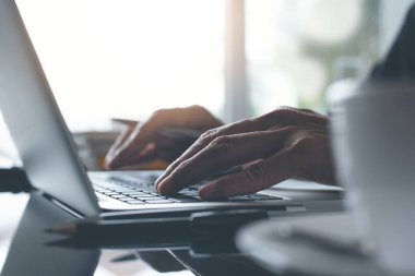 Laptop bilgisayarında çalışan bir adam kahve dükkanında ya da sabah güneşli bir ofiste bir fincan kahveyle kapatır. Taşınabilir ofis, çevrimiçi çalışma konsepti.