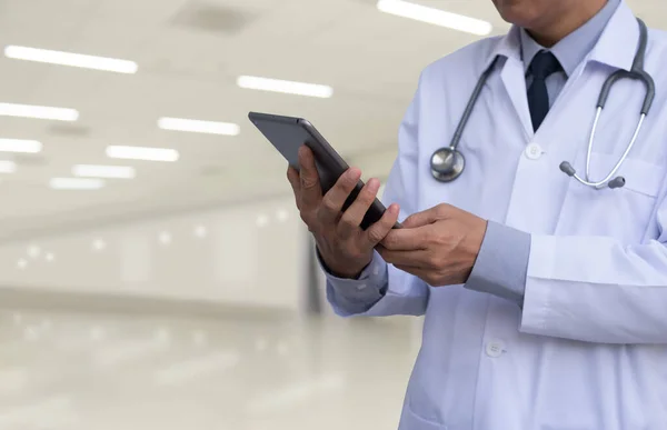 Male doctor in white coat standing and using digital tablet computer in hospital background, EHRs Electronics Health Records system, EMRs Electronics Medical Records system concept