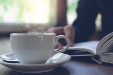 Closeup image of man reading a book. Casual business man relaxed reading book with cup of hot coffee on wooden table in coffee shop or home office in the morning, vintage tone.