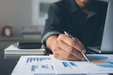 Casual businessman reviewing business report and working on laptop computer on desk. Accountants analyzing financial reports on  laptop at his office, business analytics concept.
