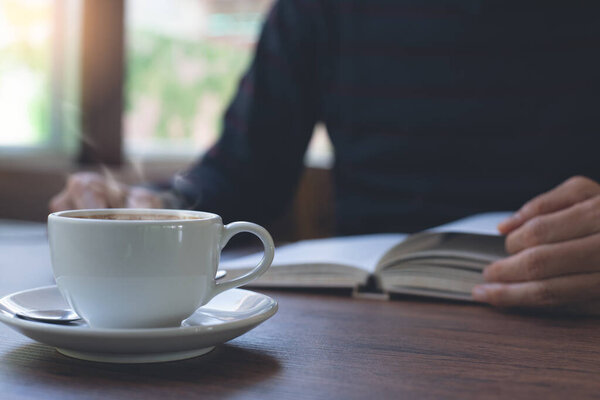 Closeup image of man reading a book. Casual business man relaxed reading book with cup of hot coffee on wooden table in coffee shop or home office in the morning, vintage tone.