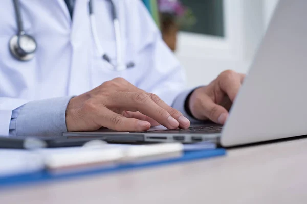 Male doctor typing on  laptop computer keyboard on office desk in doctor room, close up, telemedicine concept
