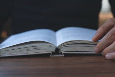 Closeup image of student reading a book in university library. Casual man opening and relaxed reading book on wooden table in coffee shop, vintage tone.