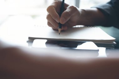 Man hand writing on papaer notebook with a pencil. Man taking note or make a plan on notepad with reflection on office desk at home, copy space, close up