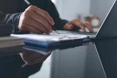 Buisness analysis concept. Businessman busy working on laptop computer, reviewing business data, financial report on desk in modern office with reflection and copy space, close up