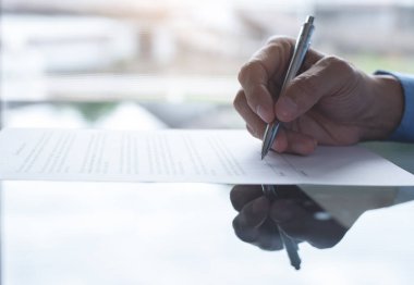 Businessperson in blue shirt reading before signing official contract. Man with pen in hand writing paper on mirror desk with copy space and reflection, close up. Deal concept