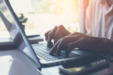 Business man or freelancer working on laptop computer on white desk with smartphone and books at home office, close up, online working, internet of things concept