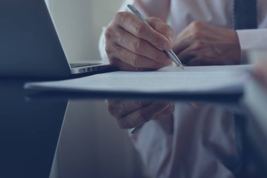 Signing contract, deal concept. Businessman reading before signing official contract with a pen and laptop computer on desk in  office. Project manager writing on business document, close up.