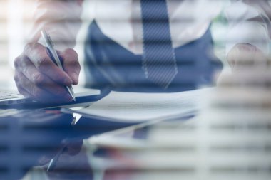 Work process concept. Businessman using calculator to calculate accountancy document with laptop computer on desk. Man executive manager hand holding a pen working with blind in privacy room in modern office, close up