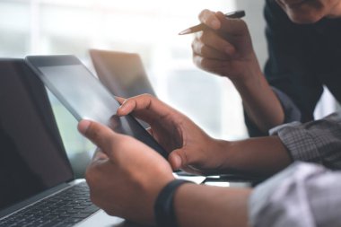 Two young business men having discussion, consulting, using digital tablet, working on laptop computer at modern office. Businessmen sharing ideas, teamwork concept. Close up