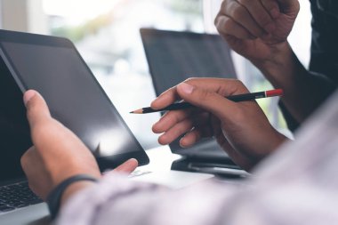 Two young business men having discussion, consulting, using digital tablet, working on laptop computer at modern office. Businessmen sharing ideas, teamwork concept. Close up