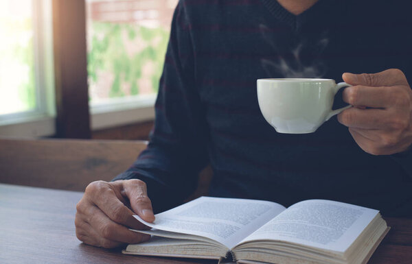 Closeup image of student reading a book. Casual business man relaxed reading book and drinking coffee on wooden table in coffee shop or home office in the morning, vintage tone. Education concept