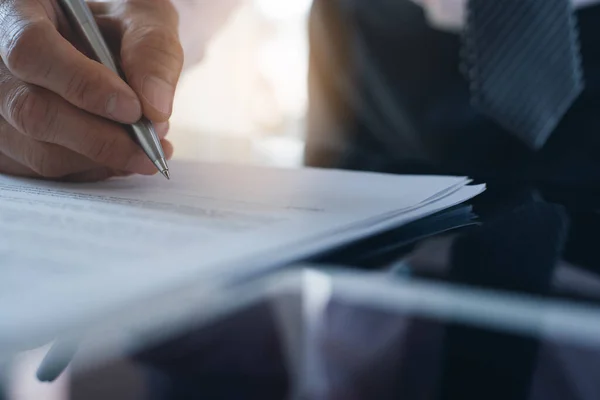 Work process and deal concept. Businessman with pen in hand reading official business contract before making a deal.  Man project manager signing document on desk in office, close up.