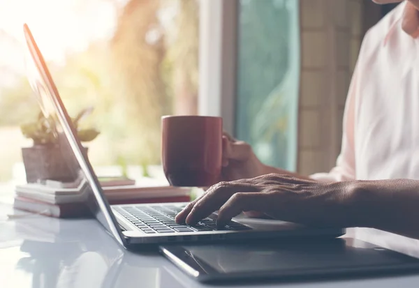 Business man working on laptop computer and drinking coffee in late afternoon, close up, vintage style.