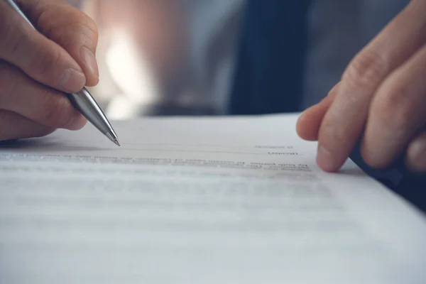 Work process and deal concept. Businessman with pen in hand reading official business contract, rental agreement before making a deal. Man project manager signing document in office, close up.